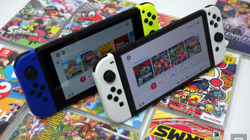 Two Nintendo Switch consoles sitting upright on an array of game boxes. Standard model with blue and yellow Joy-Cons on the left, OLED model with white Joy-Cons on the right.