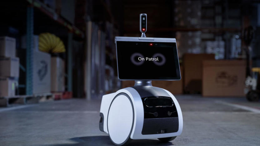 Security robot (screen with wheels and a periscope) sitting in a dark warehouse.